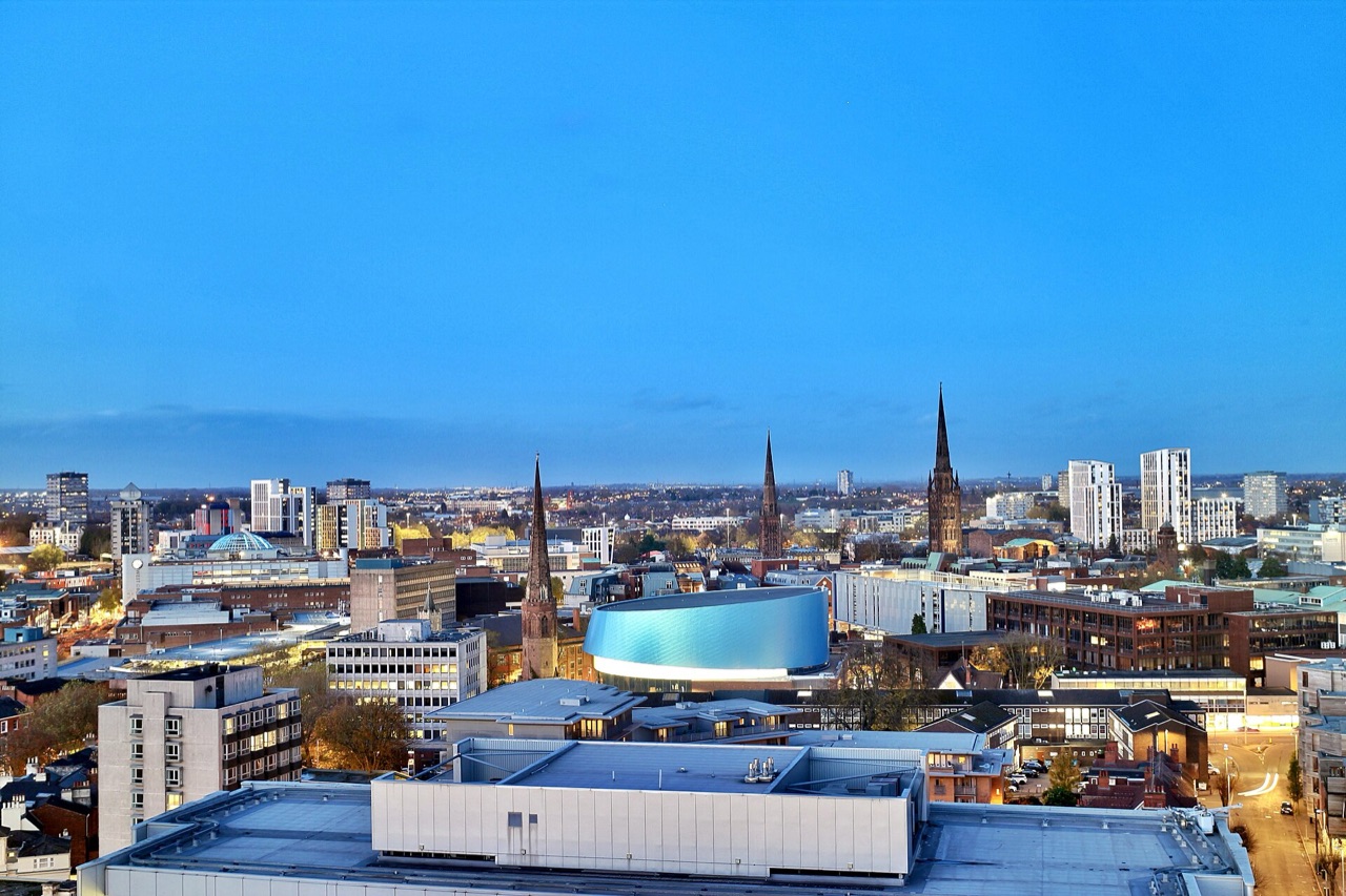 An elevated view across Coventry city centre at dusk, with church spires on the skyline